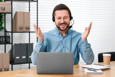 Interpreter in headset having video chat via laptop at wooden table indoors clipart