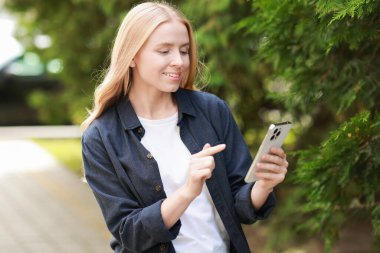 Ağacın yanında akıllı telefon kullanan gülümseyen bir kadın.