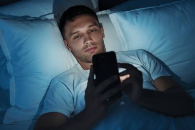 Kötü alışkanlık. Adam gece yatakta akıllı telefon kullanıyor.