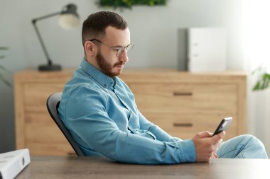 Ofiste akıllı telefona bakan yakışıklı bir adam.