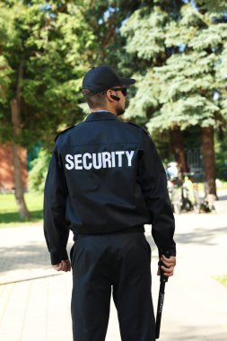 Üniformalı güvenlik görevlisi, dışarıda coplu, arkadan görüşlü.