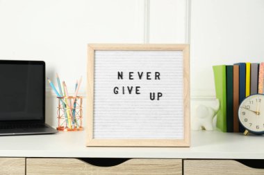 Asla pes etme, dizüstü bilgisayar, çalar saat ve kırtasiye malzemesi beyaz masada.