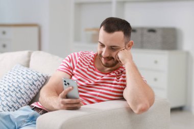 Kanepede akıllı telefon kullanan yakışıklı adam.