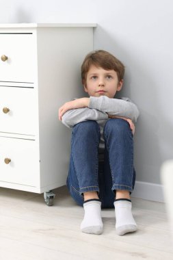 Autism concept. Lonely little boy on floor near grey wall at home clipart