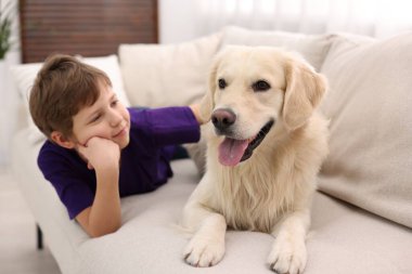 Evdeki kanepede sevimli köpeğiyle oturan çocuk.