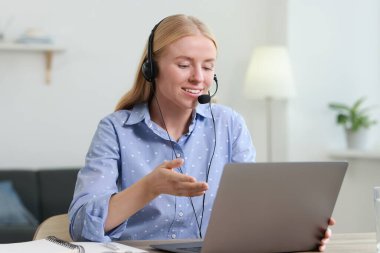 Interpreter in headset having video chat via laptop at table indoors clipart