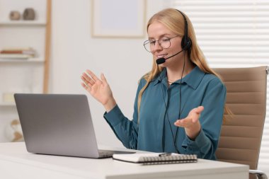 Interpreter in headset having video chat via laptop at table indoors clipart