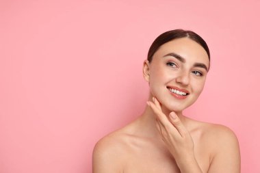 Yüz masajı. Pembe arka planda sağlıklı cildi olan güzel genç bir kadın.