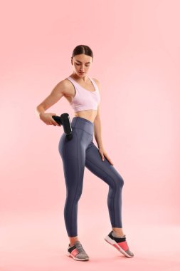 Pembe arka plandaki kalça kaslarını gevşetmek için perküsyon masaj aleti kullanan kadın.