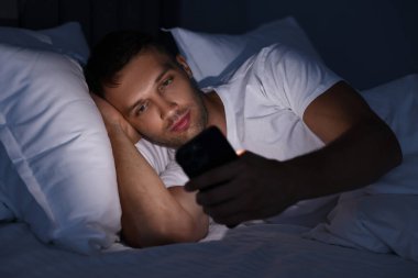 Kötü alışkanlık. Adam gece yatakta akıllı telefon kullanıyor.