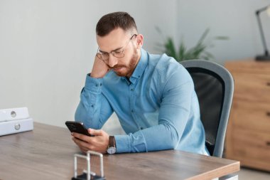 Ofiste akıllı telefona bakan yakışıklı bir adam.