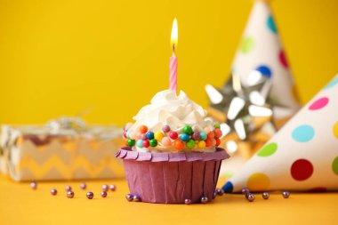 Doğum günü pastası, yanan mum ve sarı masada parti konisi.