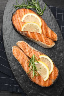 Koyu ahşap masada limonlu ve biberiyeli ızgara somon bifteği.