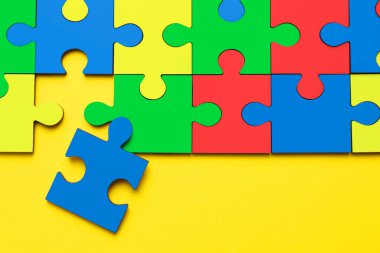 Many colorful puzzle pieces on yellow background, top view. Symbol of autism clipart