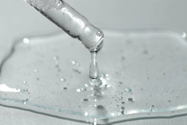 Işık arkaplanındaki pipetten akan kozmetik serumu, yakın plan