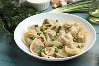 Mavi ahşap masada servis edilen yeşil soğanlı leziz pelmeni.