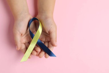 Pembe arka planda sarı ve mavi kurdeleli bir çocuk. Down sendromu farkındalığı