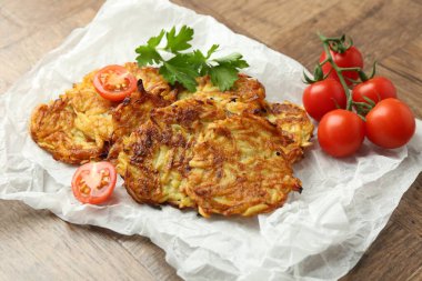 Delicious potato pancakes, tomatoes and parsley on wooden table, closeup clipart