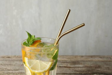 Lezzetli, ferahlatıcı bir bardak içki ve ahşap masa üzerinde pipetler. Gri arka planda, yakın plan.