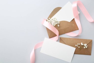 Boş kartlar, zarflar, çiçekler ve açık gri masa üzerindeki kurdele, düz yatak. Metin için boşluk