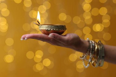 Diwali kutlaması. Renkli arka planda yanan diya lambasını tutan bulanık ışıklı kadın, yakın plan