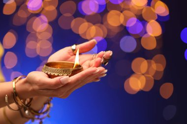 Diwali kutlaması. Mavili arka planda yanan diya lambası tutan kadın, yakın plan.