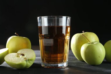 Bardakta taze elma suyu ve siyah ahşap masada meyveler, yakın plan.