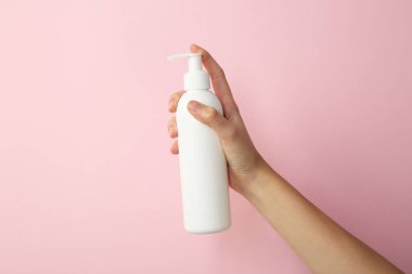 Pembe arka planda şampuan şişesi olan kadın, yakın plan.