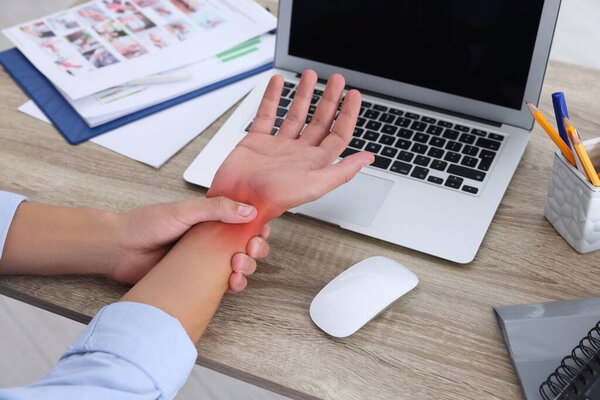 Man suffering from pain in wrist at wooden table, closeup. Office work, Carpal tunnel syndrome