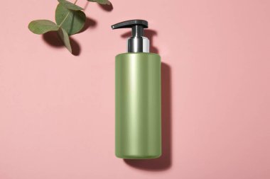 Pembe arka planda bir şişe şampuan ve okaliptüs dalı.