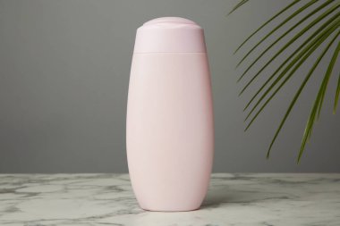 Beyaz mermer masada gri arka planda bir şişe şampuan.