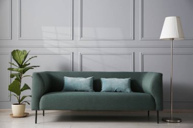 Gri duvarın yanında rahat bir kanepe, çiçek ve lamba.