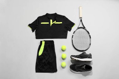 Tenis raketi, toplar ve spor kıyafetleri arka planda, düz yerde
