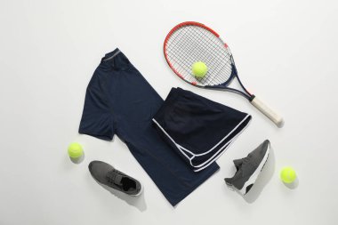 Tenis raketi, toplar, spor ayakkabıları ve arka planda spor giysileri.