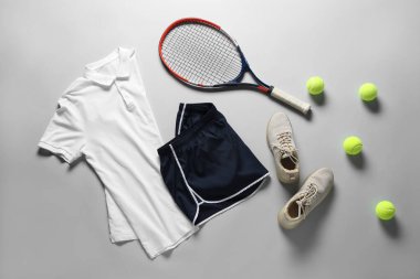 Tenis raketi, toplar, spor ayakkabısı ve gri arka planda spor giysisi, düz yatış