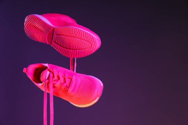 Koyu mor arka plana karşı havada şık bir çift spor ayakkabı, metin için boşluk