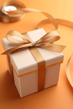 Beautiful gift box with golden bow on orange background, closeup clipart