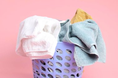 Pembe arka planda çamaşır dolu plastik sepet, yakın plan.