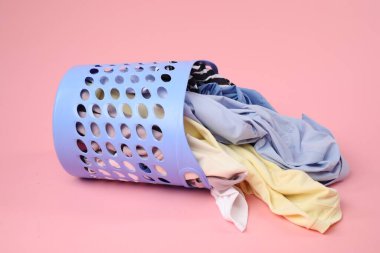 Pembe arka planda içi kıyafet dolu çamaşır sepeti devrilmiş.
