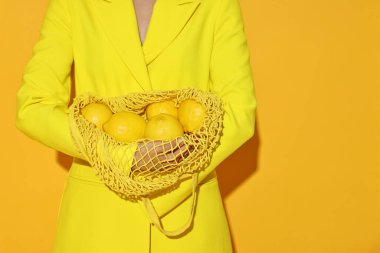 Sarı arka planda ağ çantalı ve limonlu bir kadın, yakın plan. Metin için boşluk