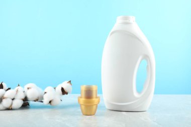 Çamaşır deterjanı şişede, kep ve pamuk çiçekleri gri mermer masada açık mavi arka planda