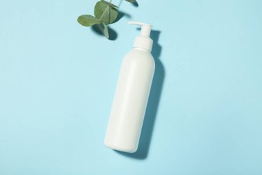 Bir şişe şampuan ve okaliptüs yaprakları açık mavi arka planda, düz yerde.