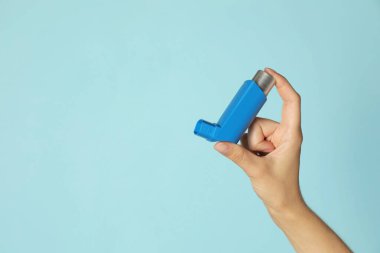 Açık mavi arka planda astım spreyi tutan kadın, yakın plan. Metin için boşluk