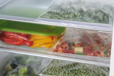 Buzdolabında farklı donmuş sebzeler olan plastik torbalar ve cam kaplar, yakın plan.