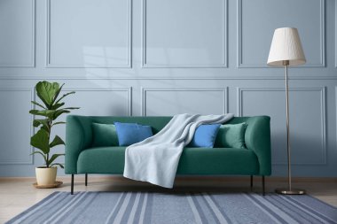 Oda duvarının yanında rahat bir kanepe, çiçek ve lamba.