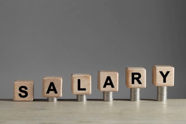 Küplerden yapılmış kelime maaşı ve gri arka plana karşı hafif ahşap masaya istiflenmiş bozuk paralar