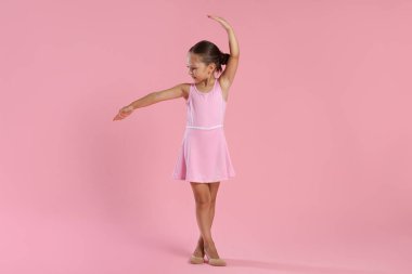 Küçük balerin pembe arka planda dans hareketleri yapıyor.