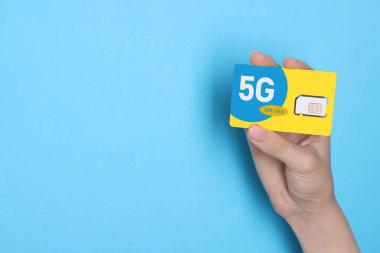 Açık mavi arka planda 5G SIM kartı tutan kadın, yakın plan. Metin için boşluk