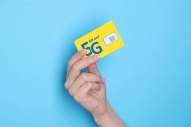 Açık mavi arkaplanda 5G SIM kartı tutan kadın, yakın plan.