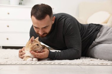 Evdeki sevimli kızıl kediyi okşayan adam.